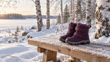 Pienet luumunväriset tarralliset talvikengät puisella penkillä lumisessa koivikossa