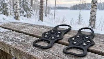Mustat irrotettavat nastalliset liukuesteet lumisen metsän puisella penkillä