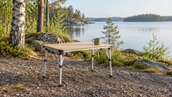 Pieni retkipöytä ja muki seisovat soralla järvenrantaleirillä