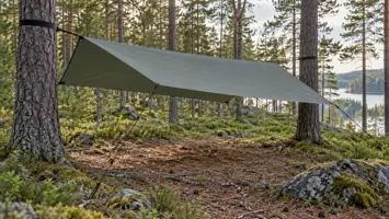 Harmaanvihreä tarppikatos kiristettynä mäntyjen väliin metsäisessä leiripaikassa